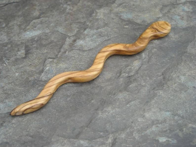 Puede incluir: Un palo de pelo de madera en forma de serpiente con un acabado de grano de madera natural. El palo es curvo y tiene una superficie lisa y pulida.