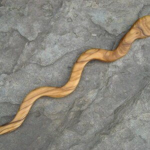 Puede incluir: Un palito para el pelo de madera con forma de serpiente, con un acabado de madera natural.