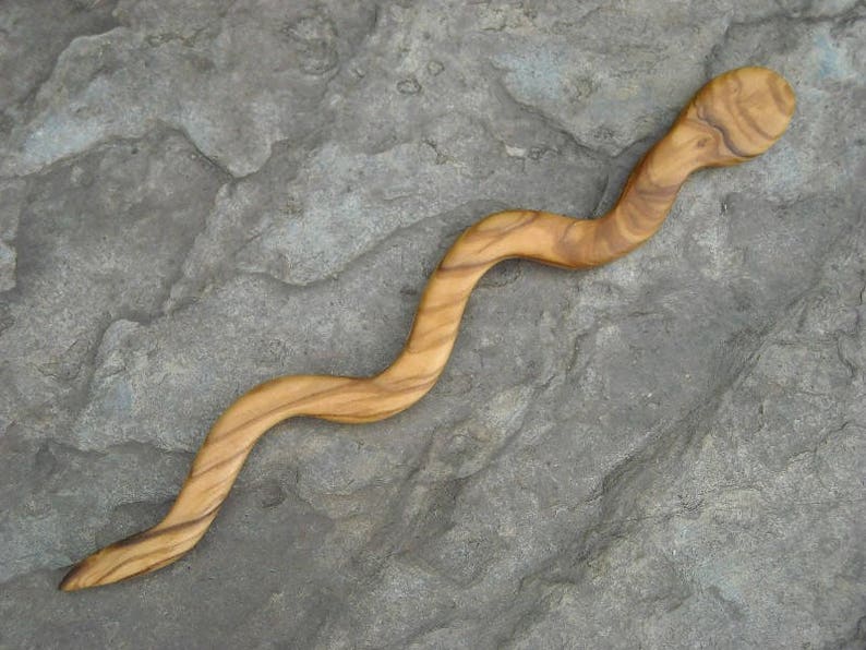 Puede incluir: Un palito para el pelo de madera con forma de serpiente, con un acabado de madera natural.