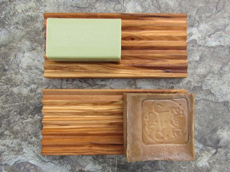 Puede incluir: Dos jaboneras de madera con un dise&ntilde;o acanalado. La jabonera superior tiene una barra de jab&oacute;n verde claro y la jabonera inferior tiene una barra de jab&oacute;n marr&oacute;n con un dise&ntilde;o en relieve.