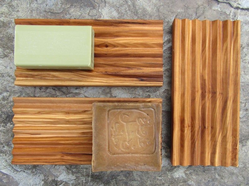 Puede incluir: Tres jaboneras de madera con superficies acanaladas. La jabonera superior tiene una barra de jab&oacute;n verde, la jabonera del medio tiene una barra de jab&oacute;n marr&oacute;n y la jabonera inferior est&aacute; vac&iacute;a.