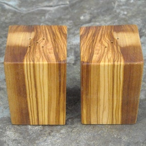 May include: A set of two wooden salt and pepper shakers with a natural wood grain finish. The shakers are square in shape and have a small hole on the top for dispensing salt and pepper.