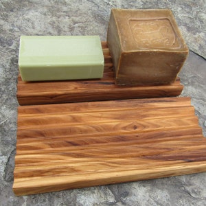 Puede incluir: Un jabonera de madera con dos barras de jab&oacute;n. La jabonera est&aacute; hecha de madera marr&oacute;n claro con un dise&ntilde;o acanalado. Una barra de jab&oacute;n es verde y la otra es marr&oacute;n.