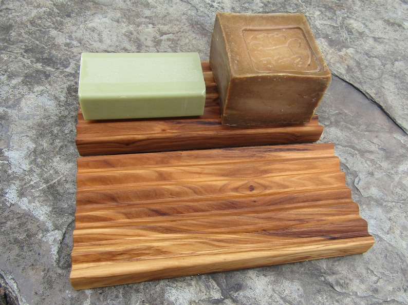 Puede incluir: Un jabonera de madera con dos barras de jab&oacute;n. La jabonera est&aacute; hecha de madera marr&oacute;n claro con un dise&ntilde;o acanalado. Una barra de jab&oacute;n es verde y la otra es marr&oacute;n.