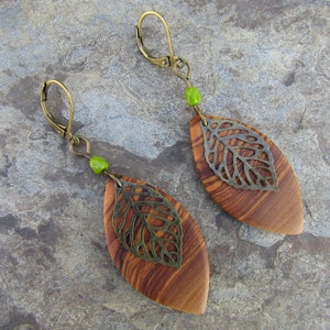 May include: A pair of wooden leaf earrings with a metal leaf design and green beads. The earrings are brown and have a natural wood grain.