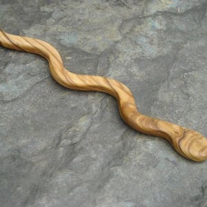 Puede incluir: Un palito para el pelo de madera con forma de serpiente, con un patr&oacute;n de veta de madera natural.
