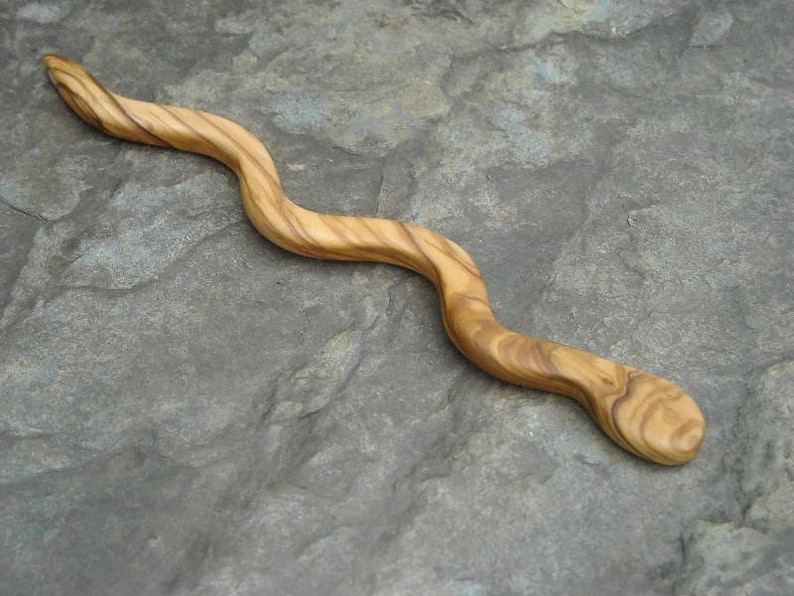 Puede incluir: Un palito para el pelo de madera con forma de serpiente, con un patr&oacute;n de veta de madera natural.