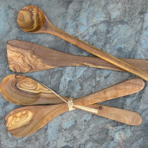 May include: Set of four wooden kitchen utensils, including a spoon, spatula, and two salad servers. The utensils are made of olive wood and have a natural, rustic finish.