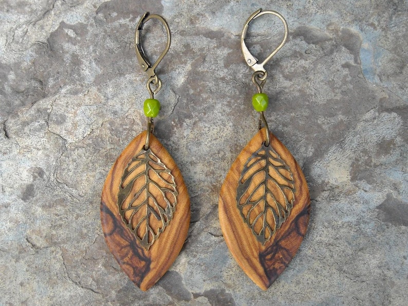 May include: Olive wood earrings with a leaf design and green glass beads. The earrings are a light brown color with dark brown streaks.