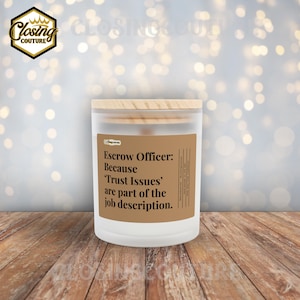 May include: A white candle with a wooden lid and a brown label. The label reads "Escrow Officer: Because 'Trust Issues' are part of the job description." The candle is on a wooden surface with a blurred background.