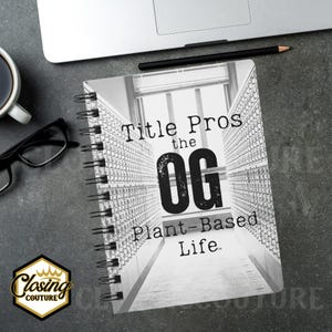 May include: A spiral-bound notebook with the text "Title Pros the OG Plant-Based Life" in black and white. The notebook's cover features a grayscale image of a hallway. A pencil and a laptop are visible.