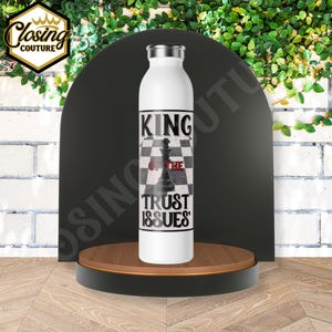 May include: White stainless steel water bottle with a black and white chessboard design and the text "King of the Trust Issues".