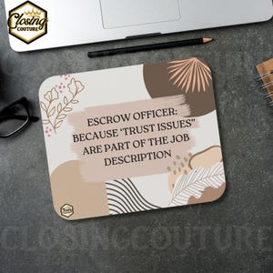 May include: A square mousepad with the text "ESCROW OFFICER: BECAUSE 'TRUST ISSUES' ARE PART OF THE JOB DESCRIPTION." The mousepad has a beige background with brown and pink abstract shapes and floral accents. A laptop and pencil are in the background.