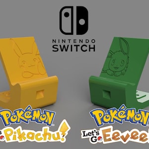 May include: Two 3D printed Nintendo Switch phone stands, one yellow with Pikachu and the other green with Eevee. The stands are designed to hold a Nintendo Switch console in a vertical position. The stands feature the Pokemon Let's Go Pikachu and Let's Go Eevee logos.