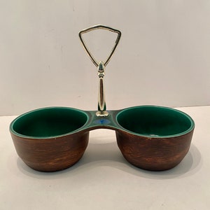 May include: A two-section serving dish with a silver handle. The dish has a brown exterior and a green interior. The handle is triangular and connects to the dish's center. The dish is likely for serving condiments or small portions.