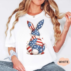 May include: White t-shirt featuring a patriotic bunny design. The bunny is made of patches of blue fabric with white stars and red and white stripes, resembling the American flag. The word "WHITE" is printed in a white bubble.
