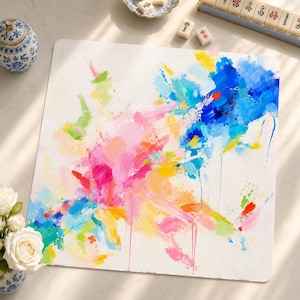 May include: A square mat featuring an abstract painting with vibrant brushstrokes in shades of pink, blue, yellow, and green on a white background. The design includes visible paint drips and textured layers of color across the surface.