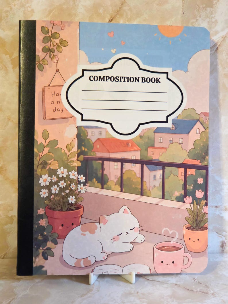 May include: A composition book featuring a cover illustration of a white cat sleeping on a balcony with potted flowers and a pink mug. The background shows a townscape under a sunlit sky. A white label with the text COMPOSITION BOOK is centred.