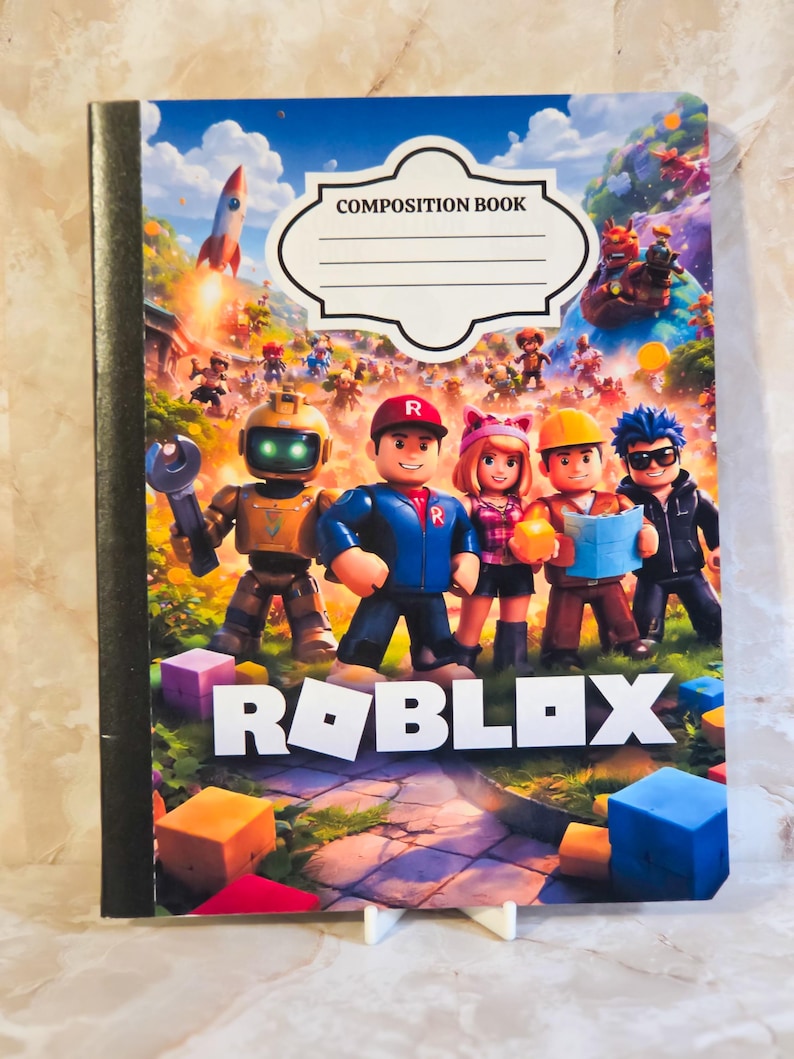 May include: A Roblox composition book featuring a colourful cover with a group of five cartoon characters, a rocket, and various blocks. The top of the cover has a white label with the text COMPOSITION BOOK and the word ROBLOX printed at the bottom.