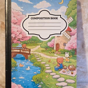 May include: A composition book featuring a colourful illustration of a landscape with a stream, a wooden bridge, a stone windmill, and cartoon bears and a rabbit having a picnic. The cover includes a white label with the text COMPOSITION BOOK.