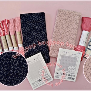 Könnte beinhalten: Eine Sammlung japanischer Sashiko-Stickutensilien, darunter Spulen mit rosa und rotem Garn, Nadeln und Stoff mit floralen Mustern. Das Bild enthält auch eine Nahaufnahme des Stoffdesigns.