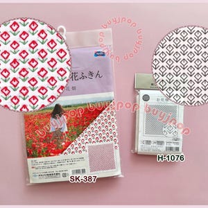 Könnte beinhalten: Das Bild zeigt zwei Packungen japanischen Stoffes, eine mit einem roten Blumenmuster und die andere mit einem schwarz-weißen geometrischen Design. Die Verpackung enthält japanischen Text und die Produktcodes SK-387 und H-1076.