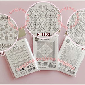 Può includere: Tre confezioni di campioni Sashiko con intricati motivi geometrici in bianco e grigio. Ogni confezione è etichettata con un nome di design diverso: Petunia, Nadeshiko e Sakura. Le confezioni sono presentate su uno sfondo rosa.