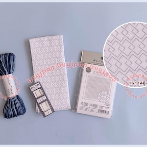 Può includere: Una collezione di forniture Sashiko, tra cui un gomitolo di filo blu navy e bianco, un tessuto bianco con un motivo geometrico, aghi e un campionario Sashiko. Un primo piano mostra il motivo del tessuto. Il testo "H-1148" è visibile.