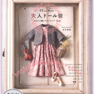May include: A framed display featuring a doll's dress and accessories. The dress is pink with a floral pattern, paired with a gray jacket. A miniature violin, basket of flowers, and white shoes complete the scene. Text includes "22 cm Size" and Japanese characters.