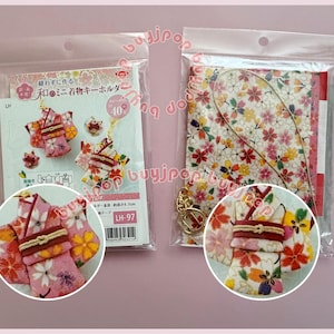 May include: Two clear plastic packages on a pink background. One contains a kit with a miniature kimono keychain, and the other contains a floral fabric and a necklace. The keychains and fabric feature colorful floral patterns.