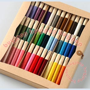 May include: A craft box filled with colorful embroidery floss. The floss is wound on paper bobbins and arranged in a variety of colors, including pink, red, yellow, green, blue, and purple. The box is made of cardboard.