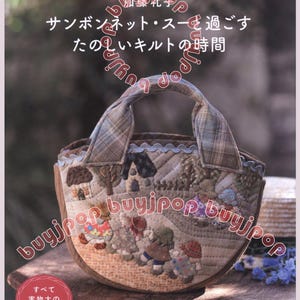 May include: A quilted handbag with a brown base and a plaid handle. The bag features a detailed landscape scene with houses and figures. The text on the cover reads "サンボンネット・スーを過ごす たのしいキルトの時間".