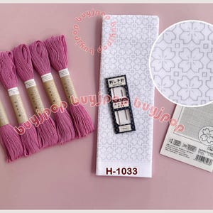 May include: A collection of embroidery items. Five pink thread skeins are arranged with a white floral patterned fabric, needles, and a sample card. The fabric has the text "H-1033".