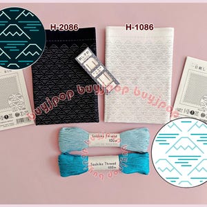 Può includere: Un assortimento di forniture per ricamo Sashiko giapponese. Include due pezzi di tessuto con motivi montani, due rocchetti di filo Sashiko e un pacchetto di aghi. I pezzi di tessuto sono neri e bianchi, e il filo è azzurro e verde acqua.