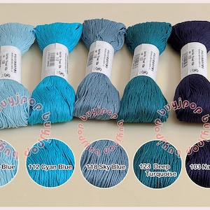 Op de afbeelding: Vijf strengen borduurgaren in blauwtinten, van lichtblauw tot marineblauw. Elke streng is gelabeld met een kleurnummer en -naam, waaronder "Lichtblauw", "Cyaanblauw", "Luchtblauw", "Diep turkoois" en "Marineblauw."