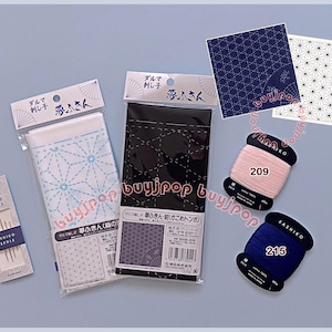 May include: A Sashiko embroidery kit featuring two fabric panels with printed geometric patterns, a pack of needles, and two spools of cotton thread in light pink and dark blue, labelled 209 and 215, with Japanese text on the packaging.