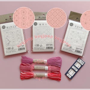 Könnte beinhalten: Eine Sammlung von Sashiko-Samplern und Stickgarn in Rosa- und Rottönen. Die Sampler zeigen florale und geometrische Muster. Ein Nadelpaket ist ebenfalls enthalten. Der Text auf der Verpackung ist auf Japanisch.