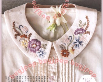 May include: A cream-colored collared shirt featuring intricate floral embroidery in shades of purple, yellow, and green on the collar. The shirt has vertical pleats down the front and a small white flower tucked into the neckline. Text in Japanese is visible.