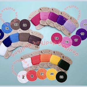 Puede incluir: Una colección de bobinas de hilo de bordar enrolladas en tarjetas de cartón, con un amplio espectro de colores que incluye blanco, azul, marrón, rosa, morado, rojo, naranja, amarillo y negro, cada una con una etiqueta numerada.