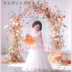May include: A doll in a white wedding dress holding an orange bouquet, standing in front of a floral arch. The book cover has the words "Wedding Dress" and "Sewing Book" in script. The book is titled in Japanese.