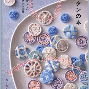 Op de afbeelding: Een verzameling handgemaakte draadknopen in verschillende kleuren en patronen, waaronder blauw, wit en perzik, gerangschikt op een lichtgrijze plaat. De afbeelding bevat ook Japanse tekst.