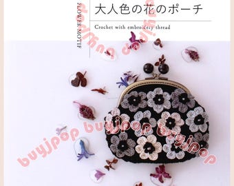 May include: A black crochet pouch with a floral design, featuring white and gray flowers. The pouch is adorned with a metal clasp and small black beads. The cover of a book is visible, with Japanese text and the words "Crochet with embroidery thread".