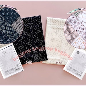 Può includere: Due quadrati di tessuto piegati con motivi geometrici di ricamo sashiko, uno blu navy scuro e uno bianco sporco, accompagnati da due confezioni di istruzioni identiche etichettate Sashiko Sampler con codici a barre e testo visibile.