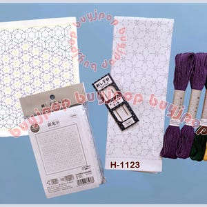 Könnte beinhalten: Eine Sammlung von japanischen Sashiko-Stickmaterialien. Enthält weißen Stoff mit geometrischem Muster, Stickgarn in Lila, Grün und Gelb, Nadeln und ein Musterpaket. Der Text "H-1123" ist sichtbar.