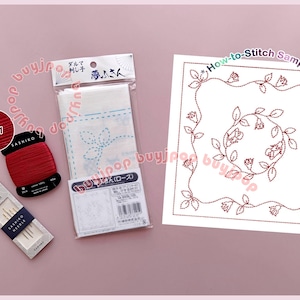Könnte beinhalten: Eine Sammlung von Sashiko-Stickzubehör, darunter rotes Garn, Nadeln und ein gedrucktes Muster mit floralem Design. Das Muster trägt die Aufschrift "How-to-Stitch Sample". Das Garn hat die Farbe 221. Die Artikel sind auf einer rosa Oberfläche angeordnet.