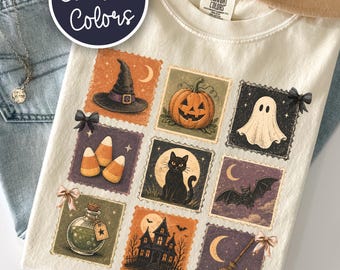 May include: A cream-colored t-shirt featuring a grid of nine square illustrations with Halloween themes, including a witch hat, jack-o'-lantern, ghost, candy corn, black cat, bat, potion bottle, haunted house, and broomstick with small bows.