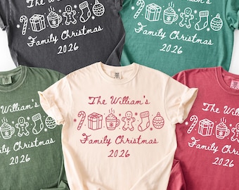 May include: Five short-sleeved crew neck t-shirts in charcoal, teal, olive green, cream, and maroon. Each shirt features white or red line art of a candy cane, gift, cocoa mug, gingerbread man, stocking, and ornament with text: The William's Family Christmas 2026.