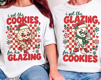 May include: Two white t-shirts featuring a red and white checkered background with Christmas-themed graphics. One shirt says "i got the COOKIES, for his GLAZING" with a cookie character, and the other says "i got the GLAZING, for her COOKIES" with a piping bag.