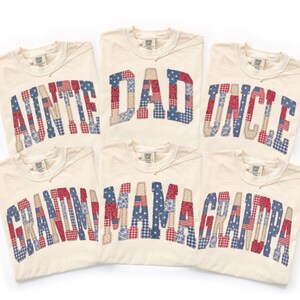 May include: Six cream-colored t-shirts with patriotic patchwork lettering spelling out "AUNTIE", "DAD", "UNCLE", "GRANDMA", "MAMA", and "GRANDPA". The letters are in red, white, and blue fabrics.