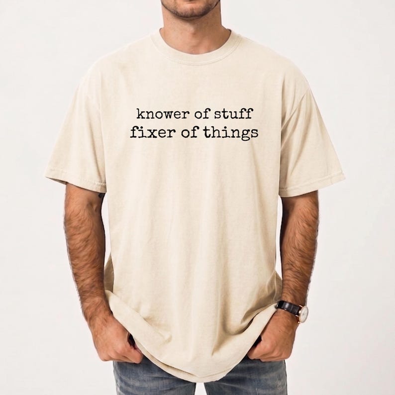 Op de afbeelding: Een beige t-shirt met de tekst "knower of stuff fixer of things" in het zwart gedrukt. Het shirt heeft korte mouwen en een ronde hals. Het shirt is gemaakt van een zacht, comfortabel materiaal.